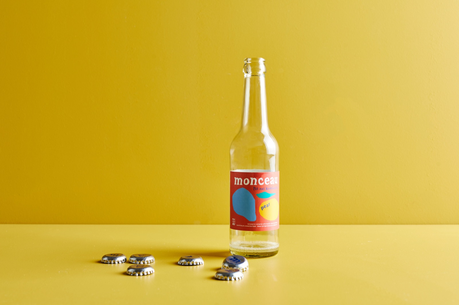 A single bottle of Monceau on a yellow backdrop with scattered bottle caps