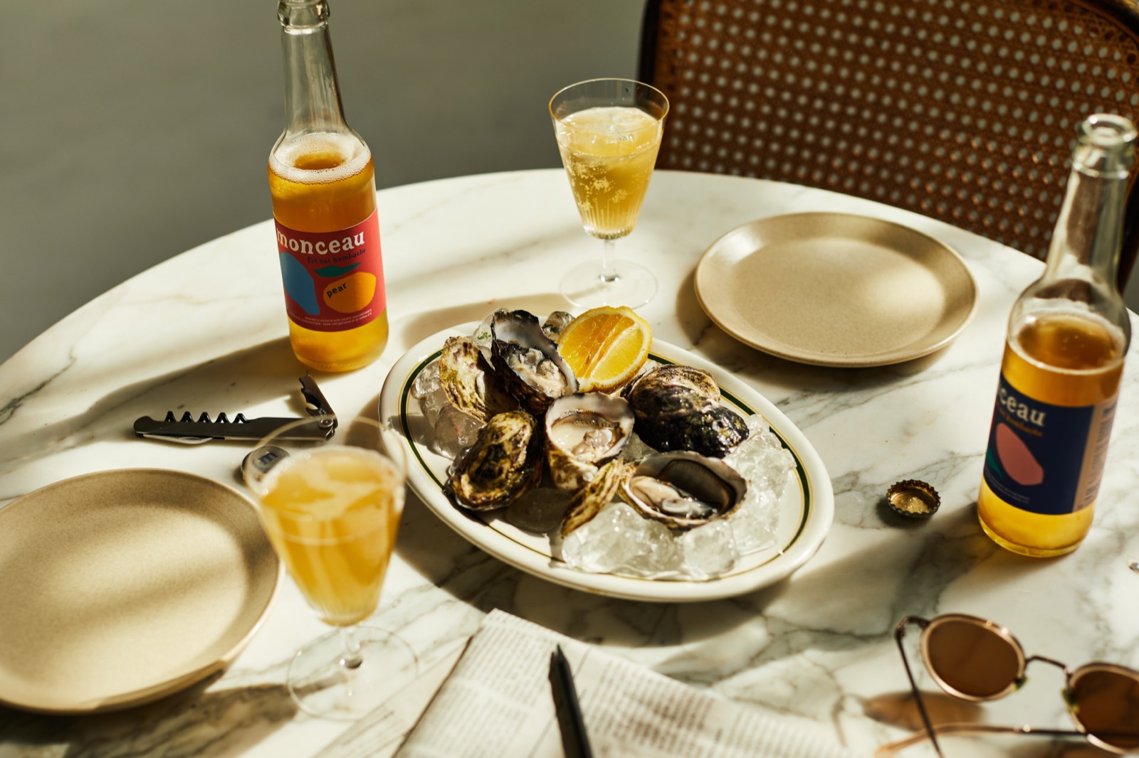 Oysters on ice, a glass of kombucha and a Monceau bottle on a marble table